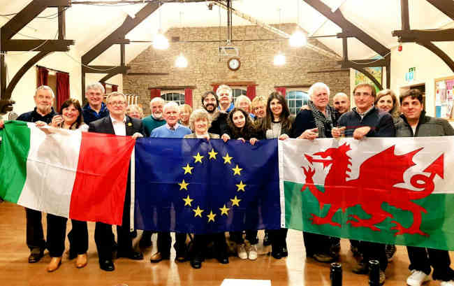 Members of the community holding flags for Italy, the EU and Wales
